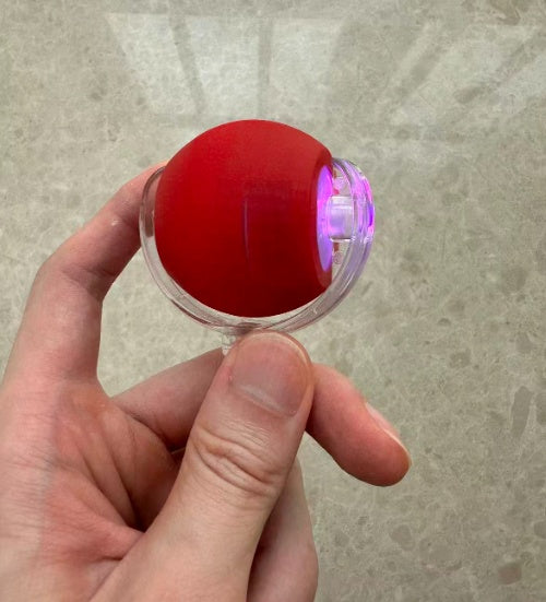 Hand holding the red rolling pet toy showing its purple LED light glowing inside