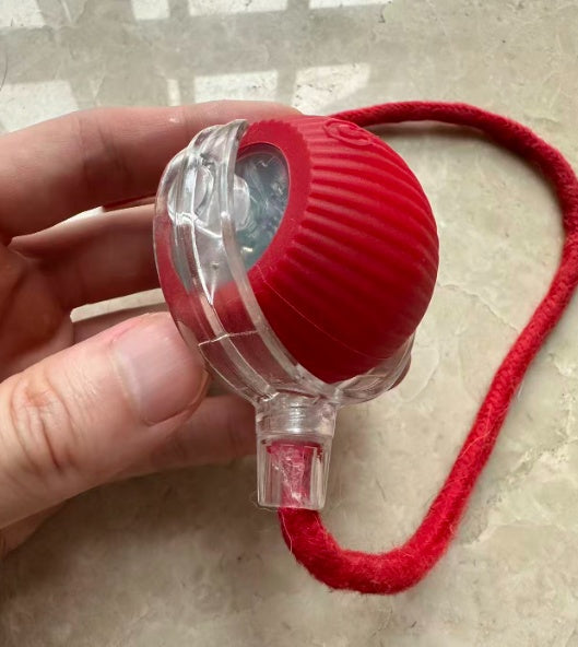 Hand holding the red rolling pet toy with rope attached, on a tile floor