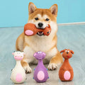 Shiba Inu holding one latex chew toy with three more animal-shaped toys beside it